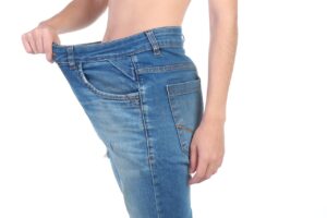 Person holding out loose jeans, suggesting weight loss success.